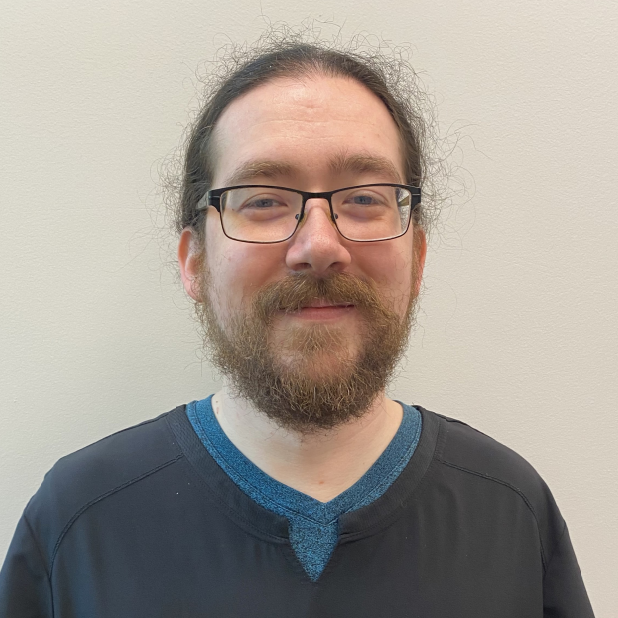Chiropractic Lacey WA Jesse Meet The Team Jesse standing in front of a white wall smiling.